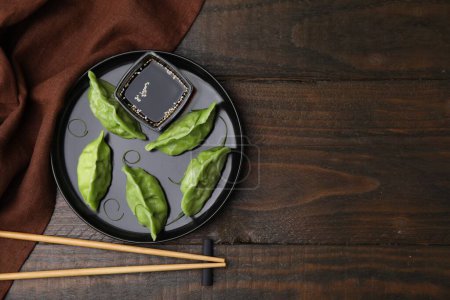 Téléchargez les photos : Délicieuses boulettes vertes (gyozas) avec sauce soja servies sur une table en bois, à plat. Espace pour le texte - en image libre de droit