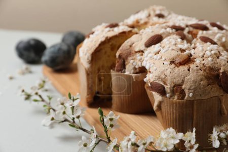 Pieces of delicious Italian Easter dove cake (traditional Colomba di Pasqua), branch with flowers and painted eggs on light grey table, closeup