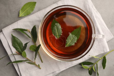 Téléchargez les photos : Tasse de thé fraîchement infusé avec des feuilles de laurier sur table grise, plat - en image libre de droit