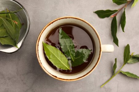 Téléchargez les photos : Tasse de thé fraîchement infusé avec des feuilles de laurier sur table grise, plat - en image libre de droit