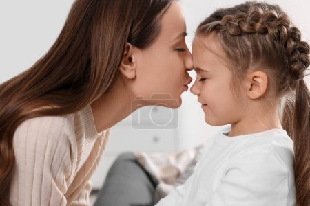 Glückliche Mutter küsst ihre süße Tochter drinnen, Nahaufnahme