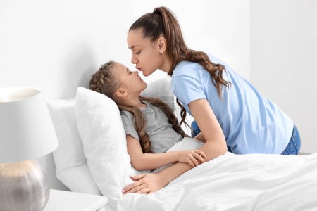 Glückliche Mutter küsst ihre süße Tochter zu Hause auf dem Bett