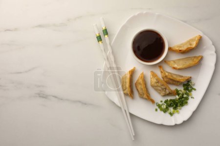 Téléchargez les photos : Délicieux gyoza (boulettes asiatiques) avec sauce soja, oignons verts et baguettes sur table en marbre blanc, vue sur le dessus. Espace pour le texte - en image libre de droit