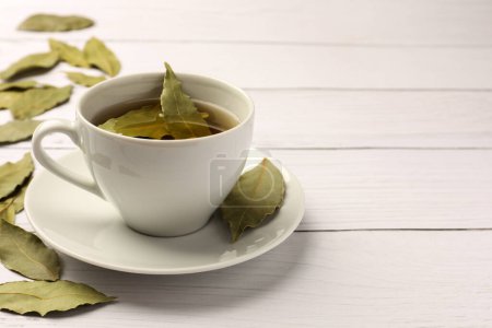 Téléchargez les photos : Tasse de thé fraîchement infusé avec des feuilles de laurier sur table en bois blanc. Espace pour le texte - en image libre de droit
