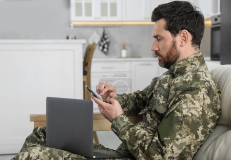 Soldat avec ordinateur portable utilisant un smartphone à la maison. Service militaire