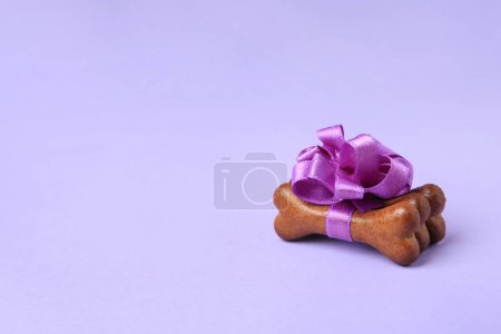 Téléchargez les photos : Biscuits pour chiens en forme d'os avec un bel arc sur fond violet, espace pour le texte - en image libre de droit