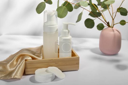 Téléchargez les photos : Bouteilles de produits nettoyants pour le visage, tampons de coton et branches d'eucalyptus sur table blanche - en image libre de droit