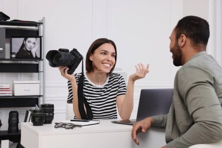 Téléchargez les photos : Jeune photographe professionnel tenant un appareil photo tout en parlant avec l'homme dans un studio photo moderne - en image libre de droit