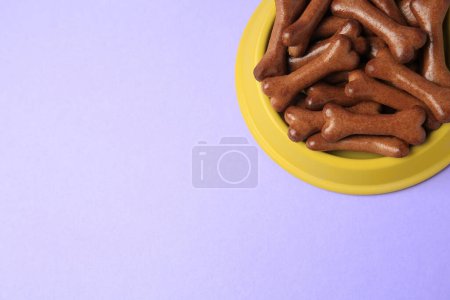 Téléchargez les photos : Bol jaune avec biscuits pour chien en forme d'os sur fond violet, vue ci-dessus. Espace pour le texte - en image libre de droit