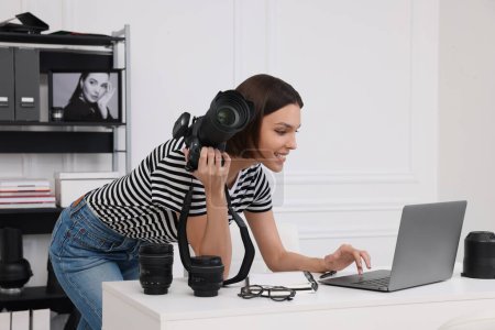 Téléchargez les photos : Jeune photographe professionnel avec appareil photo travaillant sur ordinateur portable dans un studio photo moderne - en image libre de droit