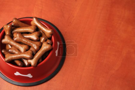 Téléchargez les photos : Bol rouge avec biscuits pour chien en forme d'os sur table en bois, espace pour le texte - en image libre de droit