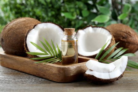 Photo for Bottle of organic coconut cooking oil, fresh fruits and leaves on wooden table - Royalty Free Image