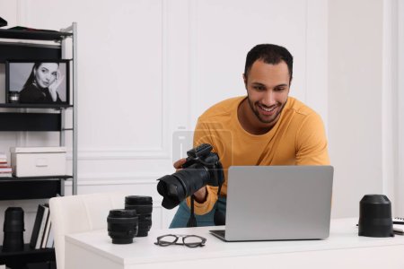 Téléchargez les photos : Jeune photographe professionnel avec appareil photo travaillant sur ordinateur portable dans un studio photo moderne, espace pour le texte - en image libre de droit