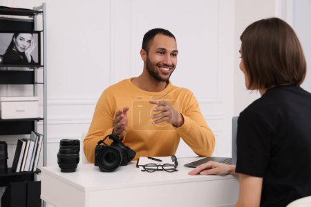 Téléchargez les photos : Jeune photographe professionnel avec appareil photo parler avec une femme dans un studio photo moderne - en image libre de droit