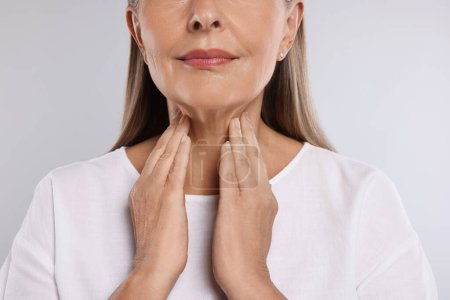Foto de Sistema endocrino. Mujer mayor haciendo autoexamen de tiroides sobre fondo gris claro, primer plano - Imagen libre de derechos