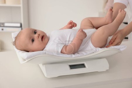 Pediatra ponderación lindo pequeño bebé en clínica, primer plano