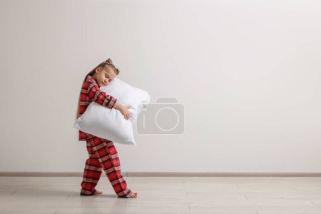 Girl in pajamas with pillow sleepwalking indoors, space for text
