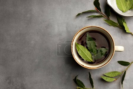 Téléchargez les photos : Tasse de thé fraîchement infusé avec des feuilles de laurier sur table grise, plat. Espace pour le texte - en image libre de droit
