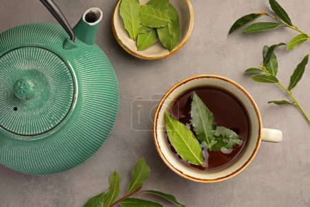 Téléchargez les photos : Tasse de thé fraîchement infusé, théière et feuilles de laurier sur table grise, plat - en image libre de droit