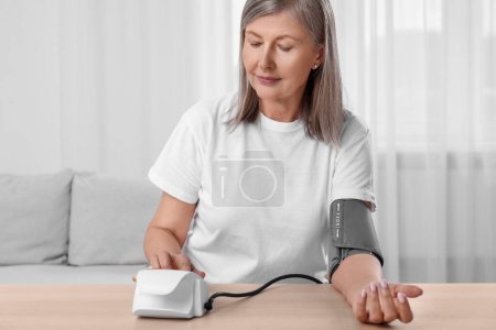 Frau misst Blutdruck an Holztisch im Zimmer