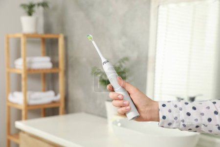 Photo for Woman holding electric toothbrush in bathroom at home, closeup - Royalty Free Image
