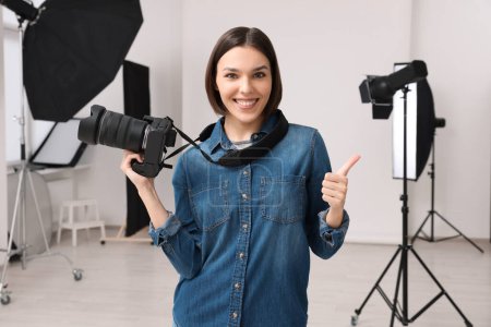 Téléchargez les photos : Photographe professionnel avec appareil photo montrant pouces vers le haut dans le studio photo moderne - en image libre de droit