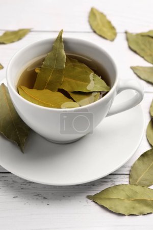 Téléchargez les photos : Tasse de thé fraîchement infusé avec des feuilles de laurier sur table en bois blanc, gros plan - en image libre de droit