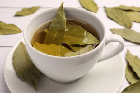 Téléchargez les photos : Tasse de thé fraîchement infusé avec des feuilles de laurier sur table en bois blanc, gros plan - en image libre de droit