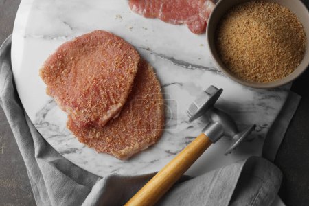 Téléchargez les photos : Schnitzel de cuisine. Côtelettes de porc crues en chapelet de pain et maillet de viande sur table grise, vue sur le dessus - en image libre de droit