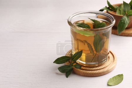 Téléchargez les photos : Coupe de thé fraîchement infusé avec des feuilles de laurier sur table en bois blanc, gros plan. Espace pour le texte - en image libre de droit