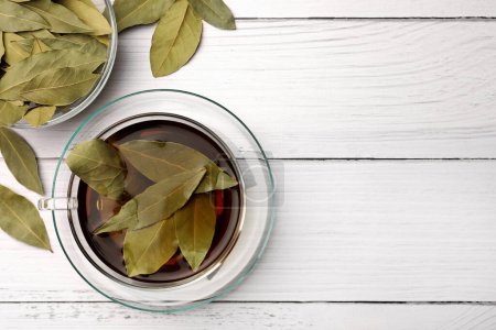 Téléchargez les photos : Tasse de thé fraîchement infusé avec des feuilles de laurier sur une table en bois blanc, plat. Espace pour le texte - en image libre de droit