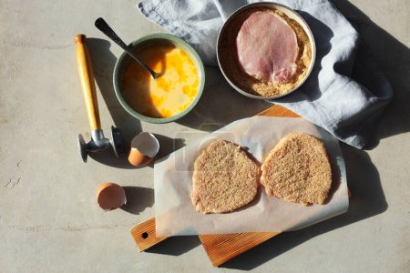 Téléchargez les photos : Schnitzel de cuisine. Côtelettes de porc crues en chapelure, maillet de viande et ingrédients sur table grise, plat - en image libre de droit