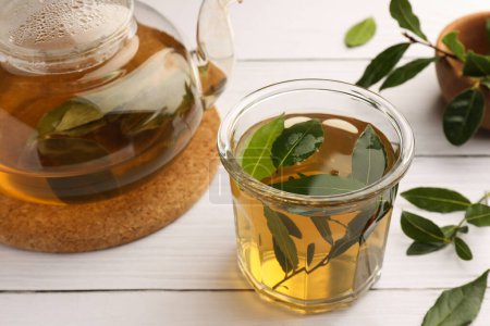 Téléchargez les photos : Coupe de thé fraîchement infusé, théière et feuilles de laurier sur table en bois blanc, gros plan - en image libre de droit