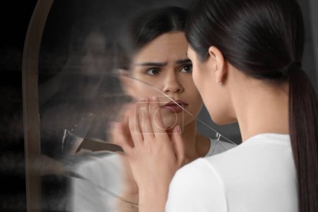 Suffering from hallucinations. Woman seeing her reflection screaming in broken mirror