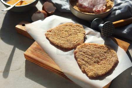 Téléchargez les photos : Schnitzel de cuisine. Côtelettes de porc crues en chapelure, maillet de viande et ingrédients sur table grise - en image libre de droit