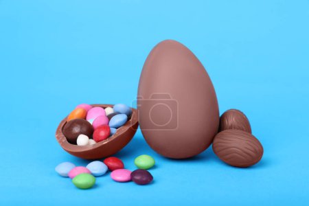 Delicious chocolate eggs and candies on light blue background, closeup