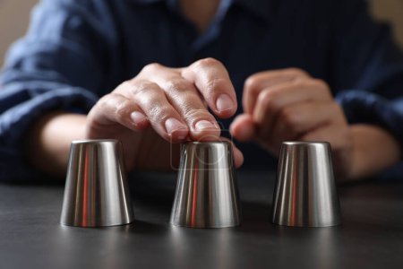 Woman playing thimblerig game with metal cups at black table, closeup
