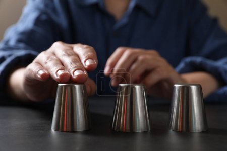 Téléchargez les photos : Femme jouant jeu de thimblerig avec des tasses en métal à la table noire, gros plan - en image libre de droit