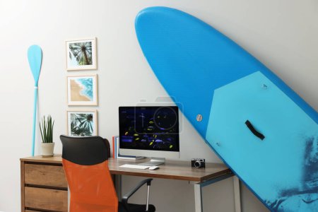 Photo for Stylish workplace with modern computer and SUP board near light wall in room. Interior design - Royalty Free Image