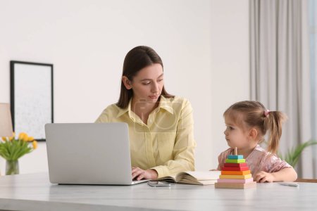 Woman working remotely. Mother with laptop and daughter at desk
