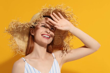 Téléchargez les photos : Belle jeune femme en chapeau de paille se ombrer avec la main de la lumière du soleil sur fond orange - en image libre de droit