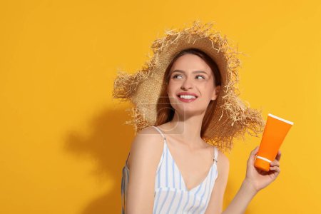 Photo for Beautiful young woman in straw hat holding sun protection cream on orange background, space for text - Royalty Free Image