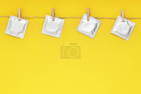Clothesline with packaged condoms on yellow background, space for text. Safe sex