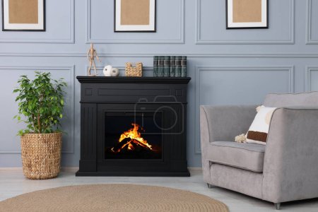 Photo for Black stylish fireplace near armchair and potted plant in cosy living room - Royalty Free Image