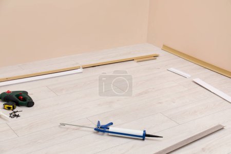Plinths, caulking gun, screwdriver, measuring tape and screws on laminated floor in room