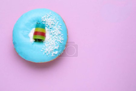 Téléchargez les photos : Donut glacé savoureux décoré avec des copeaux de noix de coco et des bonbons aigre-ciel sur fond violet, vue sur le dessus. Espace pour le texte - en image libre de droit