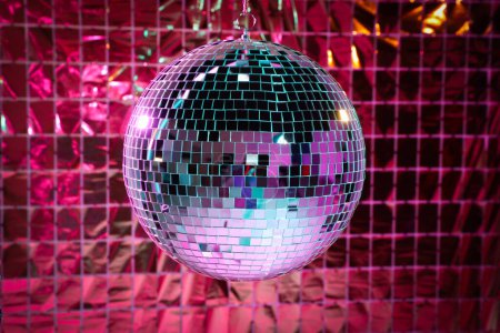 Shiny disco ball against foil party curtain under pink light