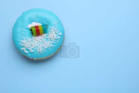 Téléchargez les photos : Donut glacé savoureux décoré avec des copeaux de noix de coco et des bonbons aigre-ciel sur fond bleu clair, vue de dessus. Espace pour le texte - en image libre de droit