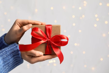 Téléchargez les photos : Femme tenant boîte cadeau avec arc rouge contre les lumières floues festives, gros plan et espace pour le texte. Effet Bokeh - en image libre de droit