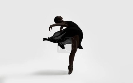 Beautiful ballerina with black veil dancing on light background. Dark silhouette of dancer